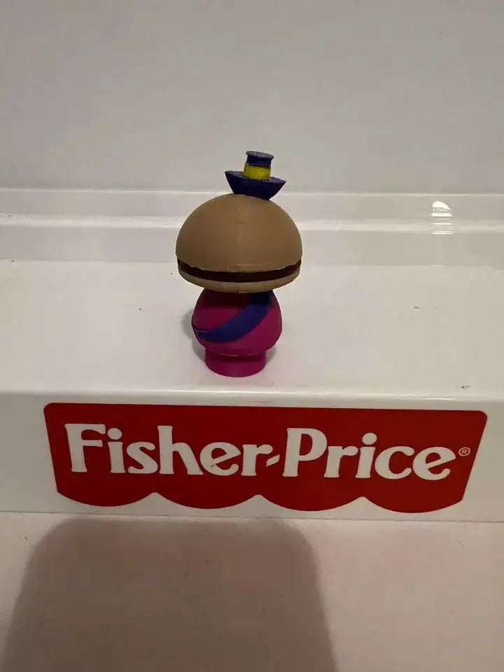 Back view of cheese-headed mayor toy figurine, brown head, magenta outfit, blue hat