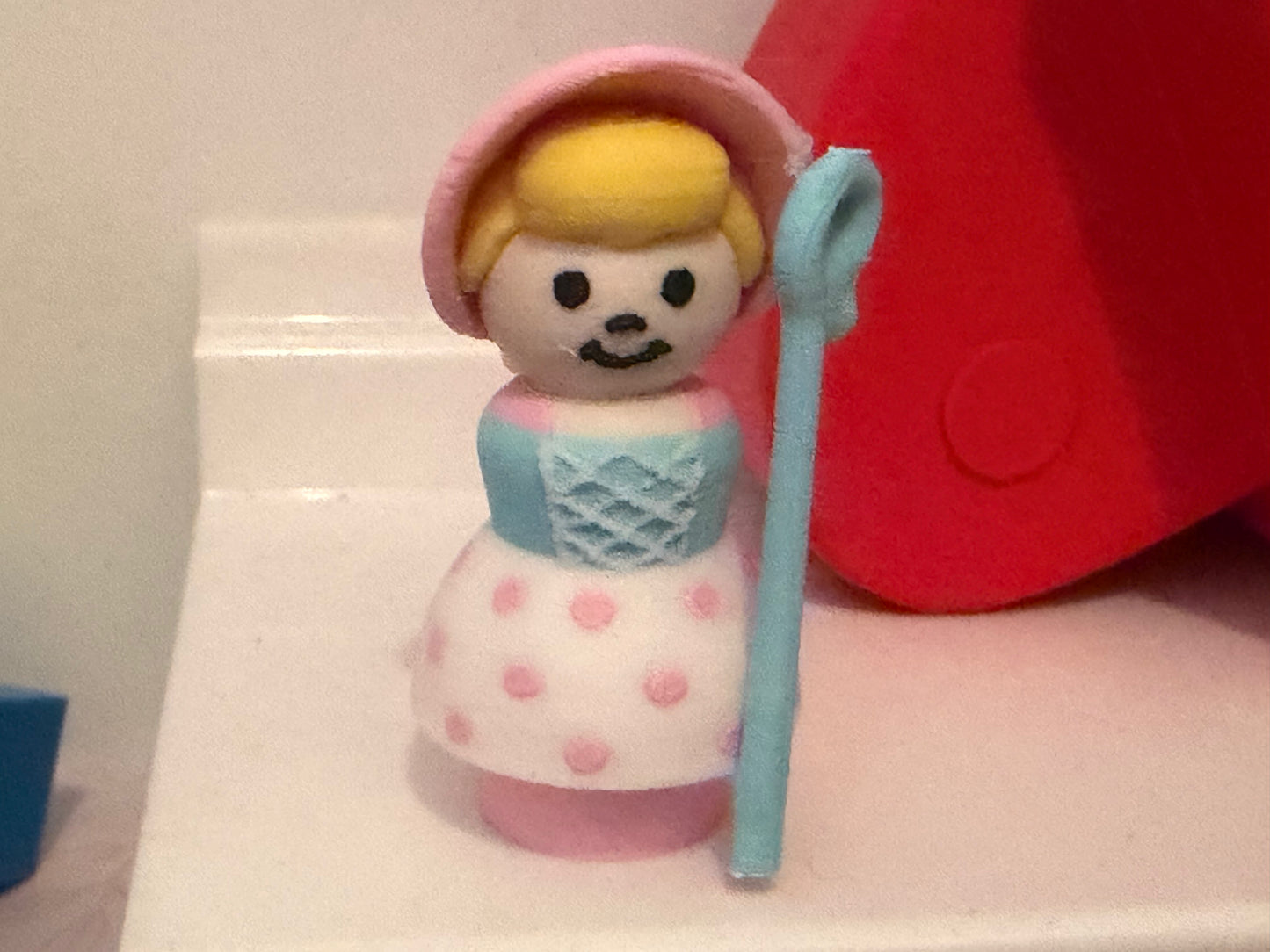Collectible figure with pink bonnet, blue dress and polka-dot skirt, holding blue staff