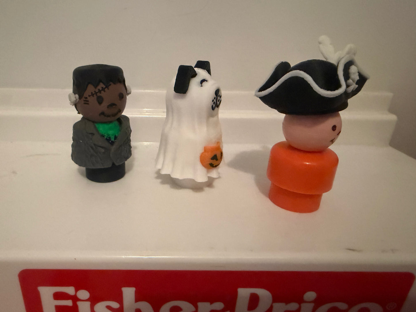 Three mini Halloween costume figures: pirate in black hat, ghost sheet, Frankenstein suit.