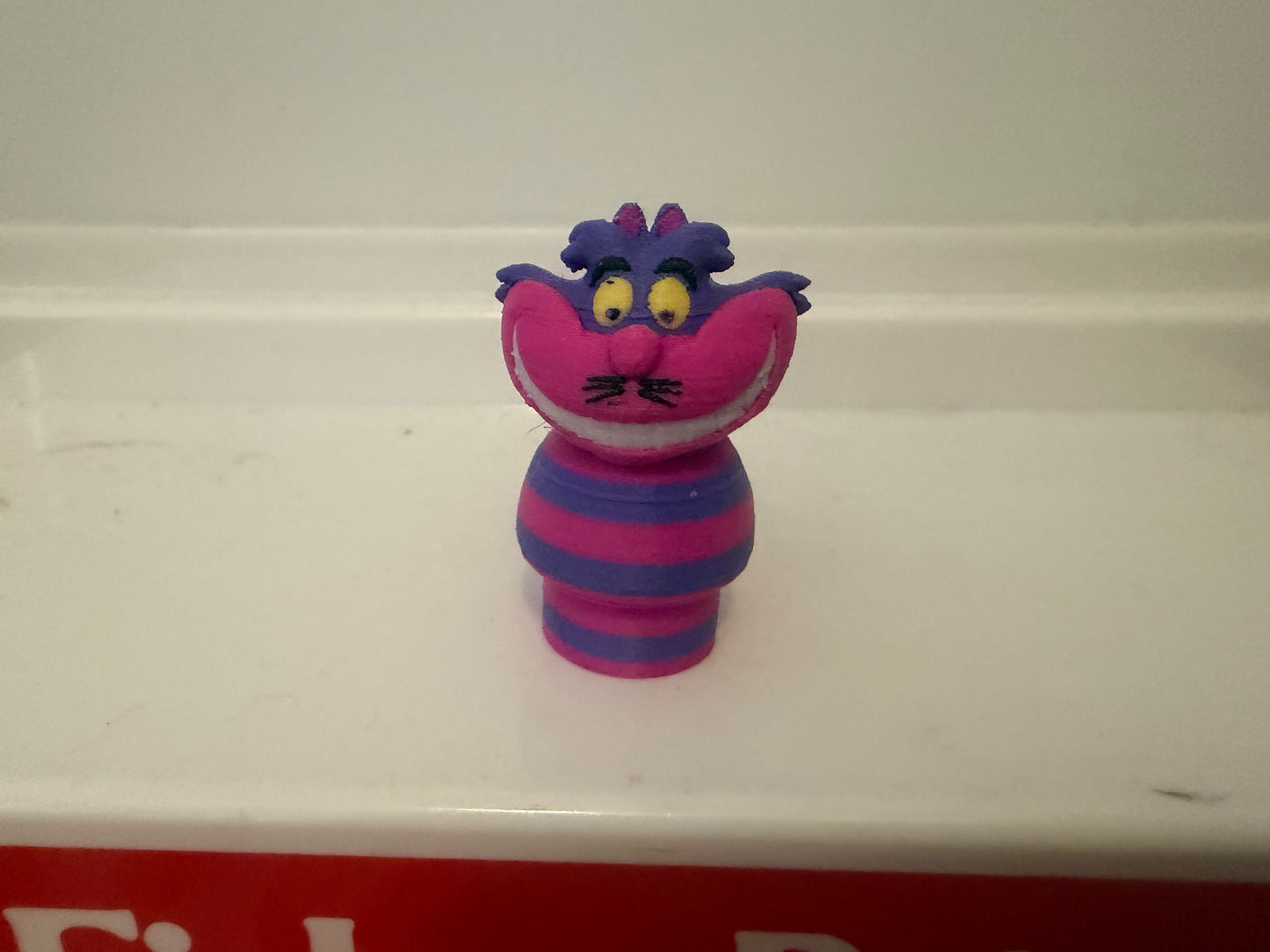 Cheshire Cat plush figure, purple head and striped blue/magenta outfit, smiling face