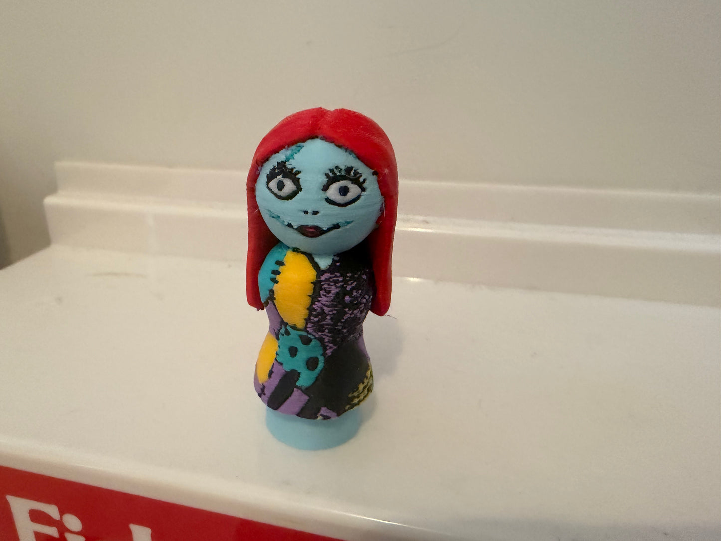 Sally collectible figure with red hood and blue face, purple patterned dress