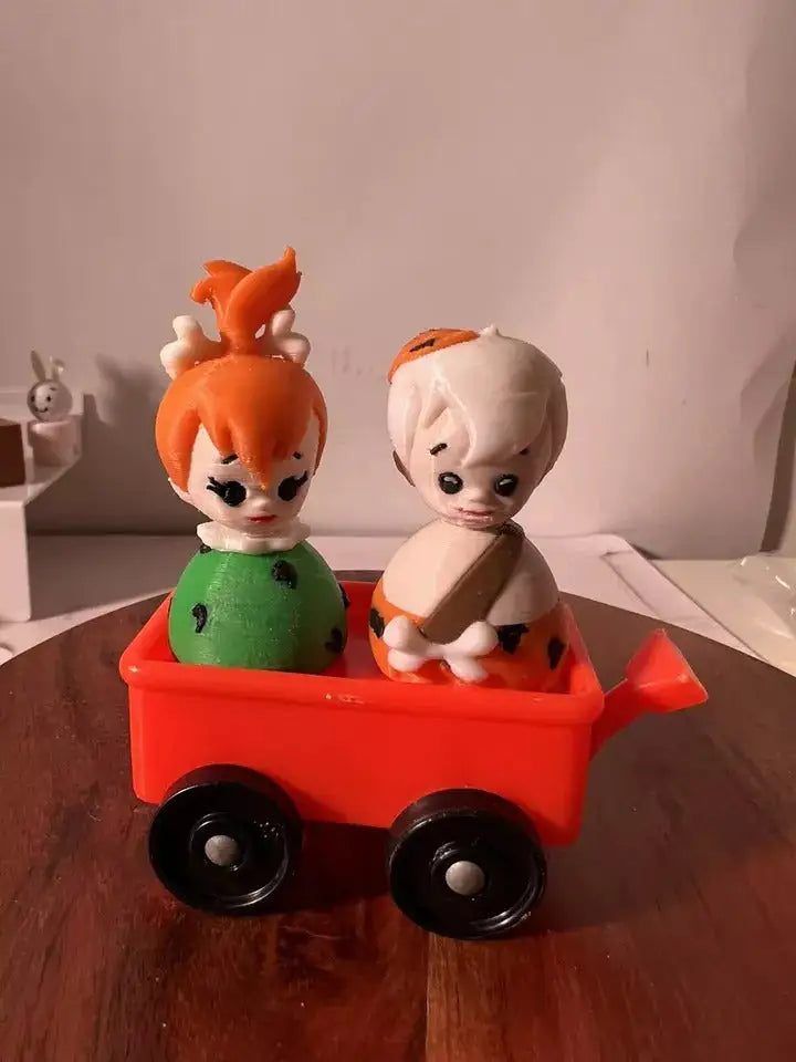 Custom 3D-printed Fisher-Price Little People figures of Pebbles and Bam Bam from The Flintstones in a red wagon.