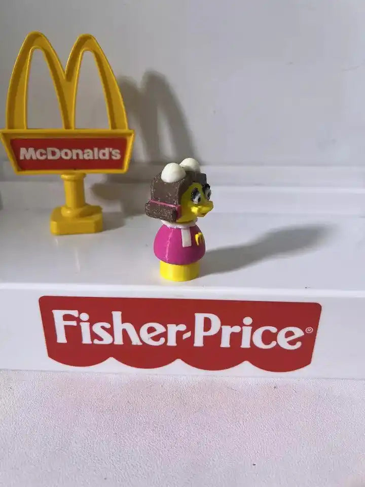 McDonald's Birdie toy figurine, side view; yellow beak, black hair, pink dress, on base
