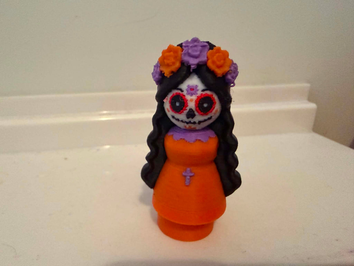 Catrina-style girl figurine front view with orange dress, skull face, and flowers