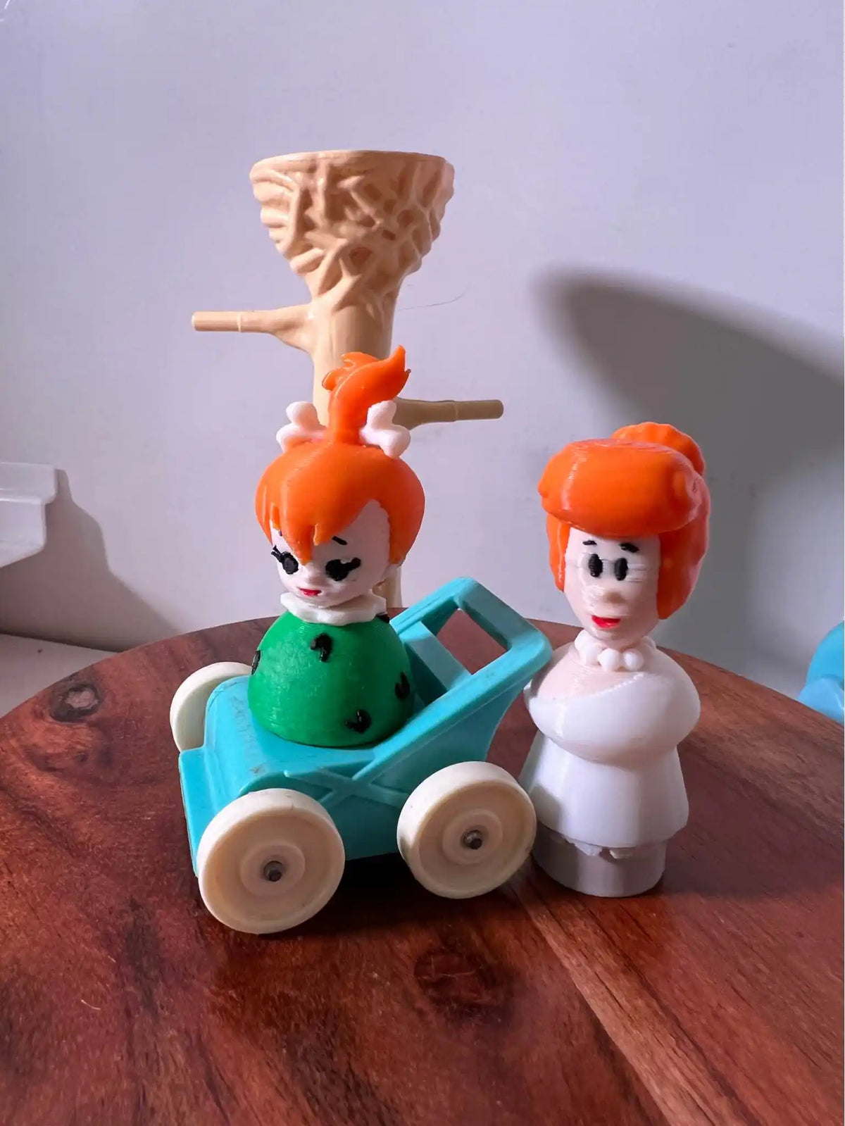 Flintstones Wilma figurine in white outfit beside an orange-haired figure on a teal cart