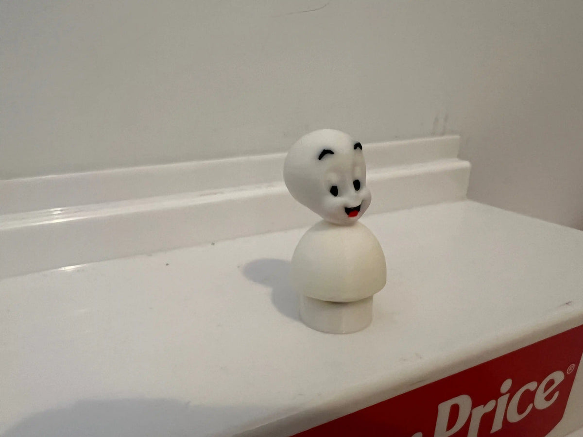 White Casper the Friendly Ghost figurine from the side, with black eyes and red smile.