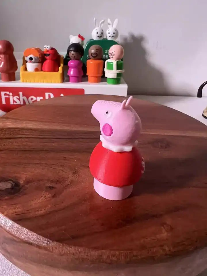 Pink pig figurine in red top and white feet, posed on wooden base