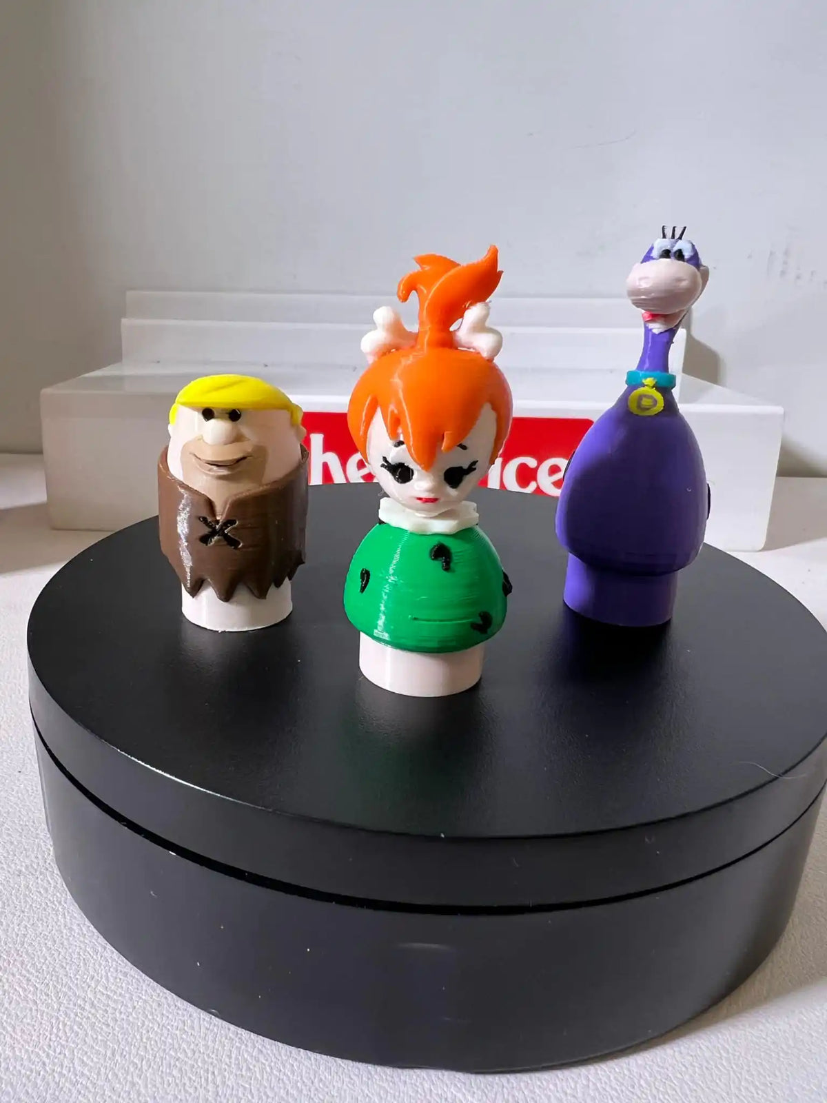 Custom 3D-printed Flintstones Little People figures (Barney, Betty, and Dino) displayed on a black rotating stand.