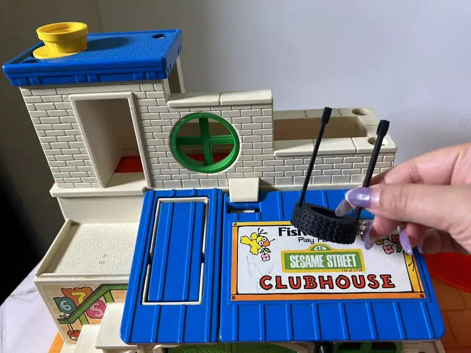 Dark gray tire swing on black stand beside blue Fisher-Price Sesame Street Clubhouse toy