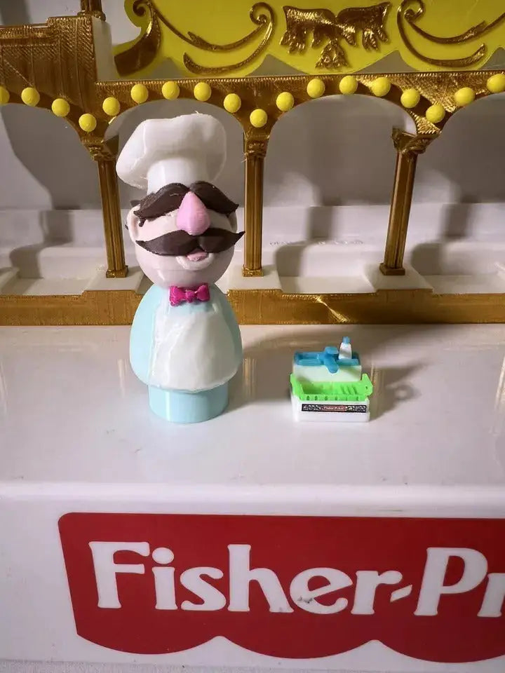 Swedish chef puppet figurine facing forward, white hat and brown mustache with pink bow tie