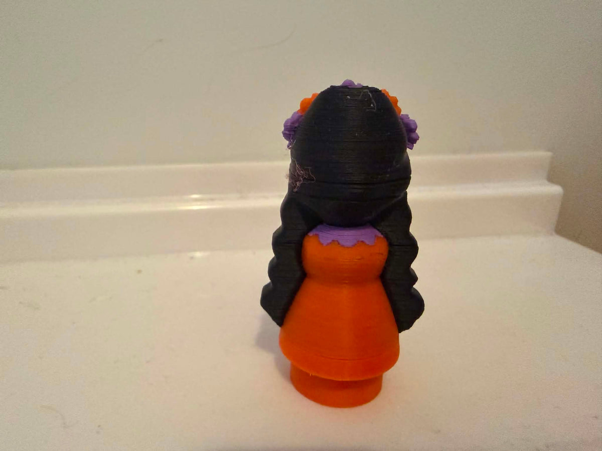 Catrina-style girl figurine back view with long black hair and orange dress