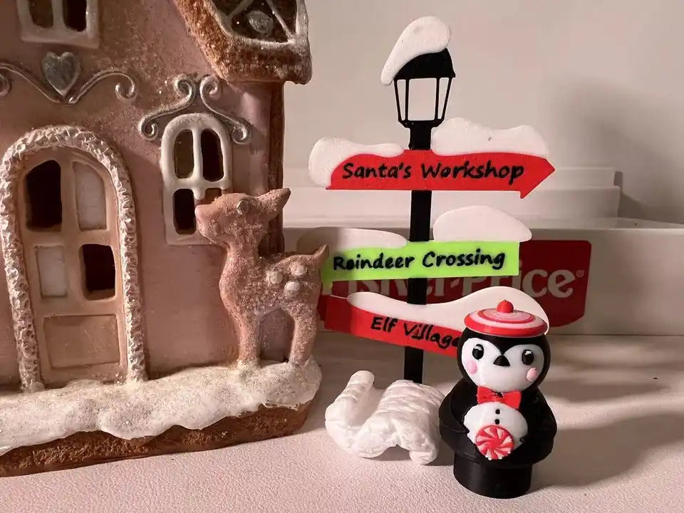 The Little People-style Peppermint Penguin figure stands beside a gingerbread house and a "Santa's Workshop" sign.