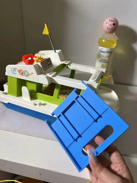 A hand holds a blue 3D-printed replacement roof for a vintage Fisher-Price Happy Houseboat