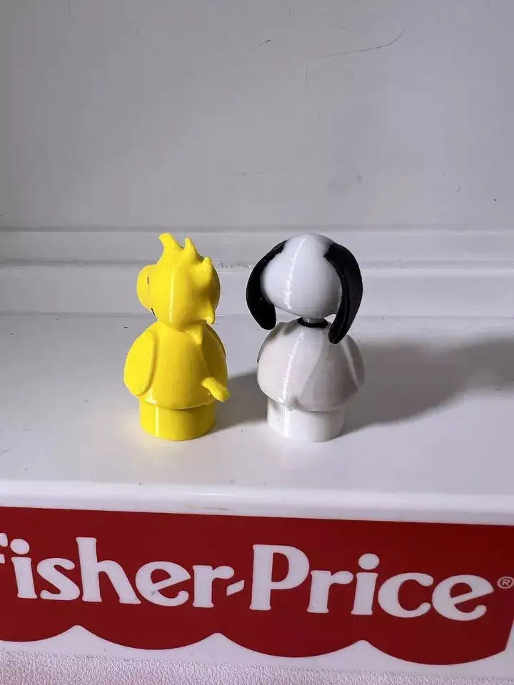 Standing Snoopy dog figurine with white body and black ear patch beside yellow character