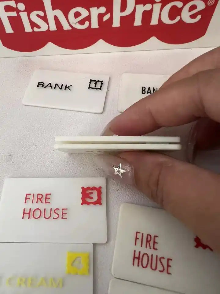 Hand holding a stack of Fisher-Price mail cards, with Bank and Fire House cards visible