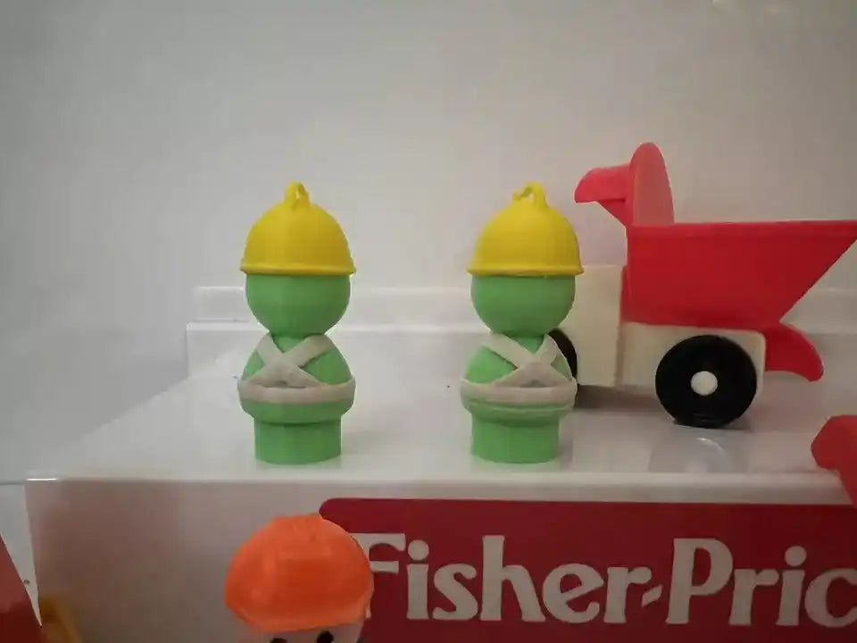 Two green Doozer figures with yellow caps beside a red toy cart with black wheel