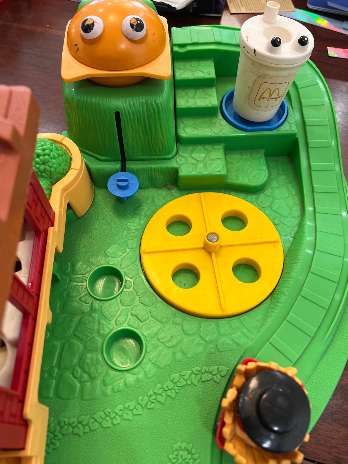 Green toy track with yellow spinner wheel and character figures beside red building