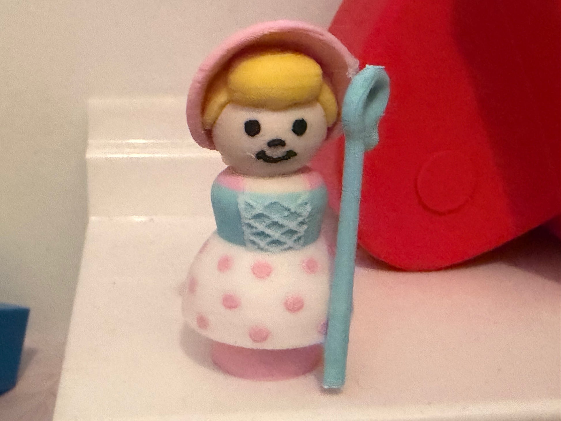 Collectible figure with pink bonnet, blue dress and polka-dot skirt, holding blue staff