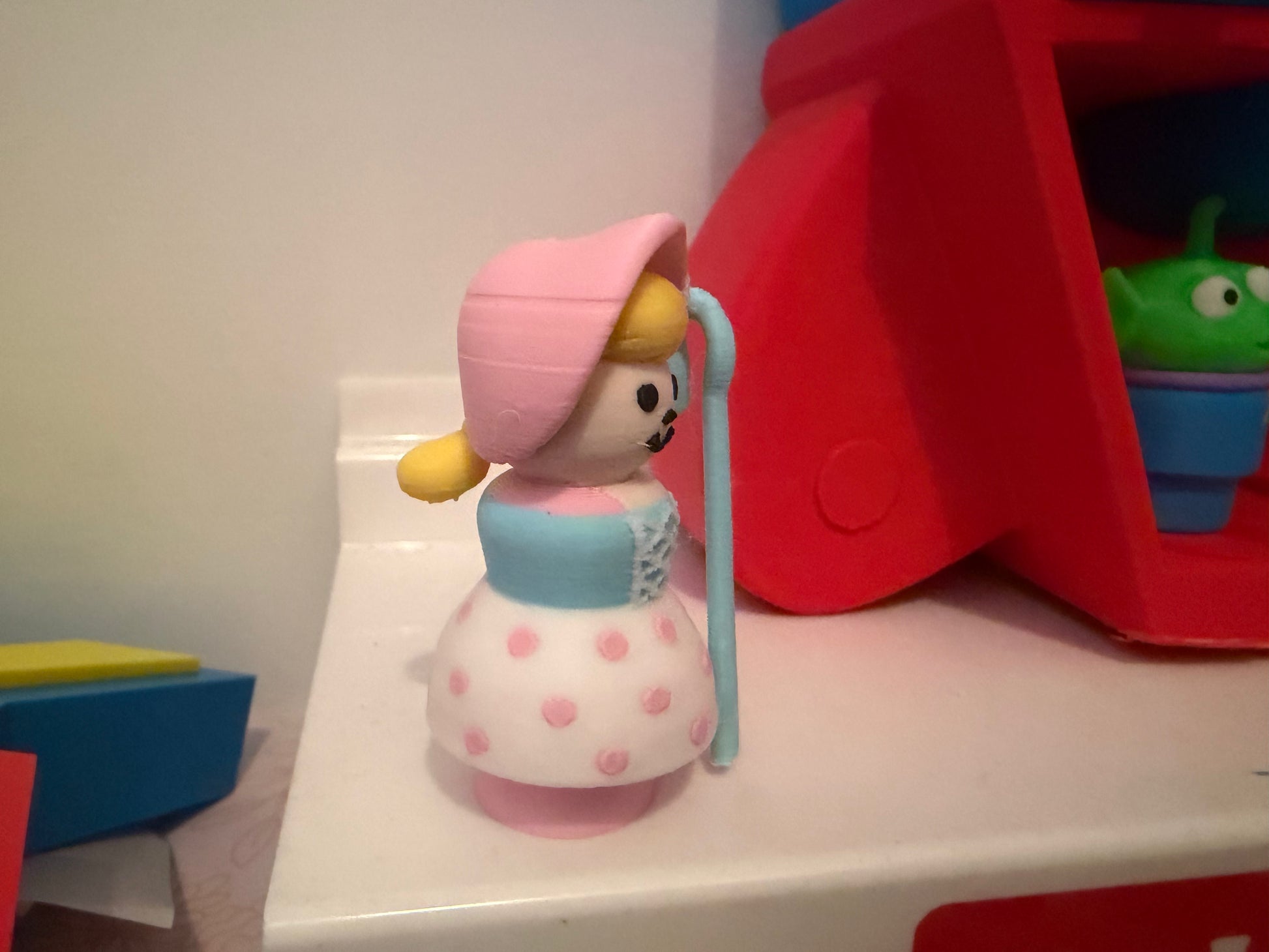 Collectible figure standing sideways, pink bonnet and blue dress with pink polka dots, staff