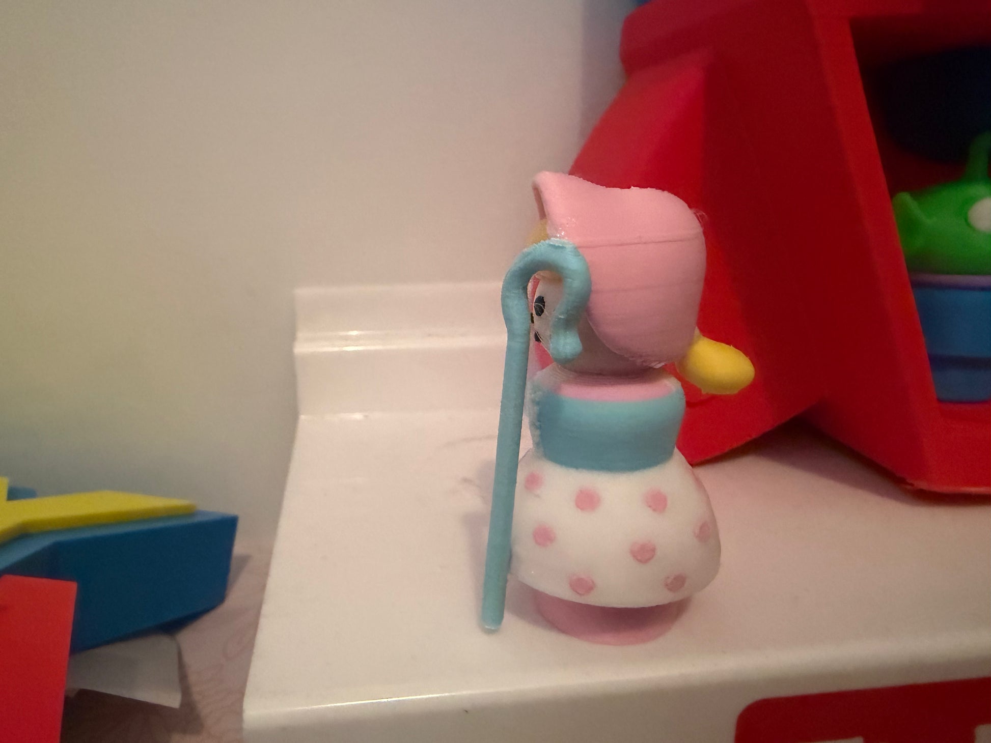 Collectible figure with pink bonnet, blue dress and pink polka-dot skirt, holding blue staff