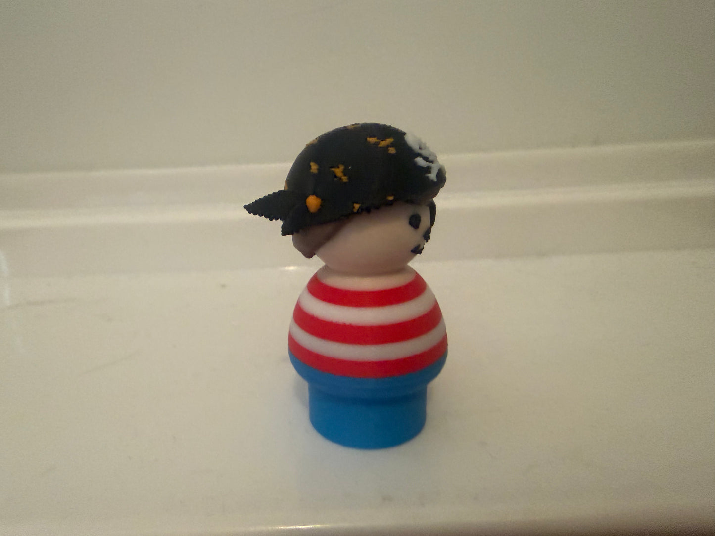 Pirate toy figure with black tricorn hat, red-and-white striped shirt, blue base