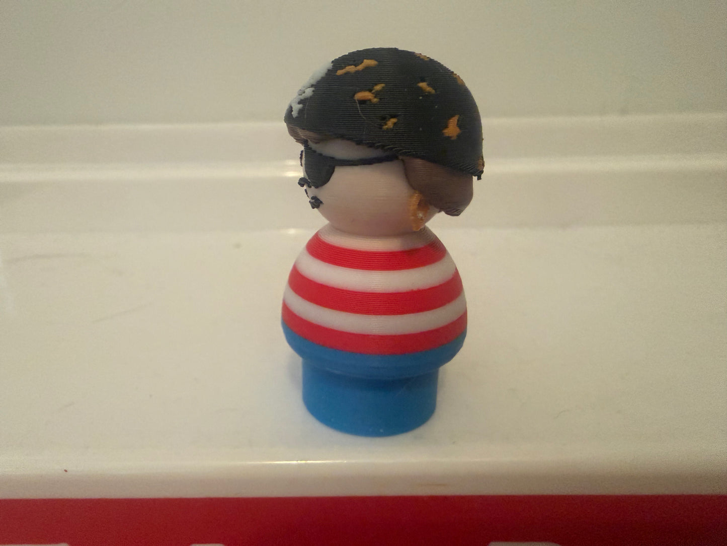 Pirate toy figure back view: black hat, red-and-white striped shirt, blue base