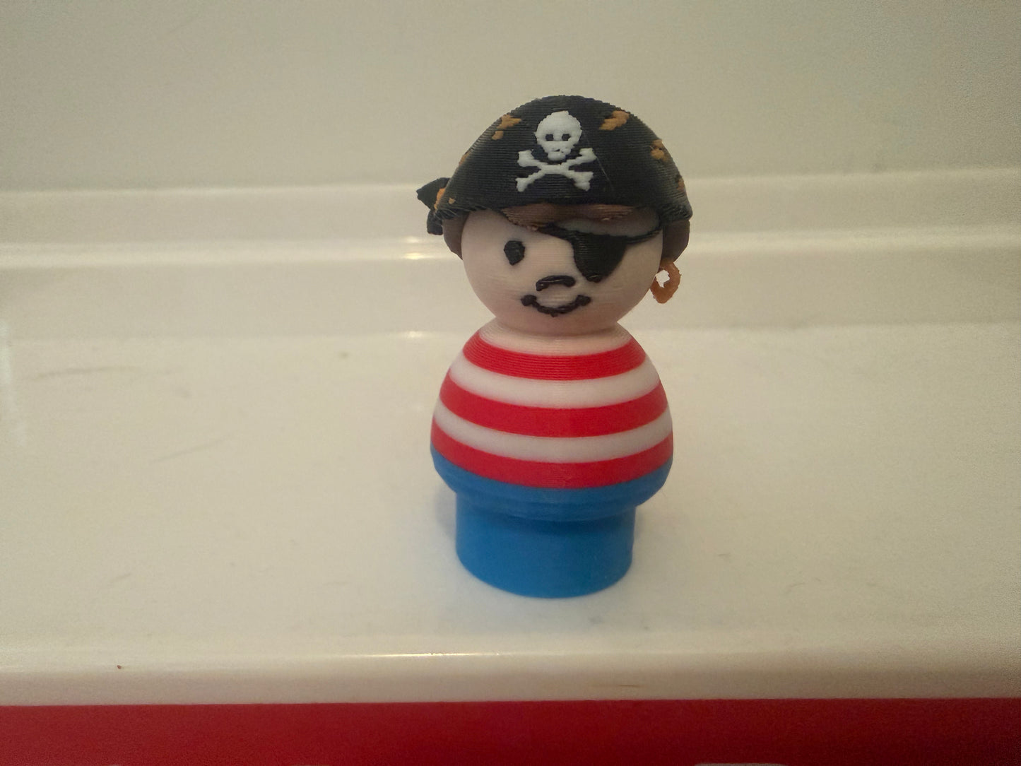 Pirate toy figure front view: black tricorn hat with skull, striped shirt, blue base