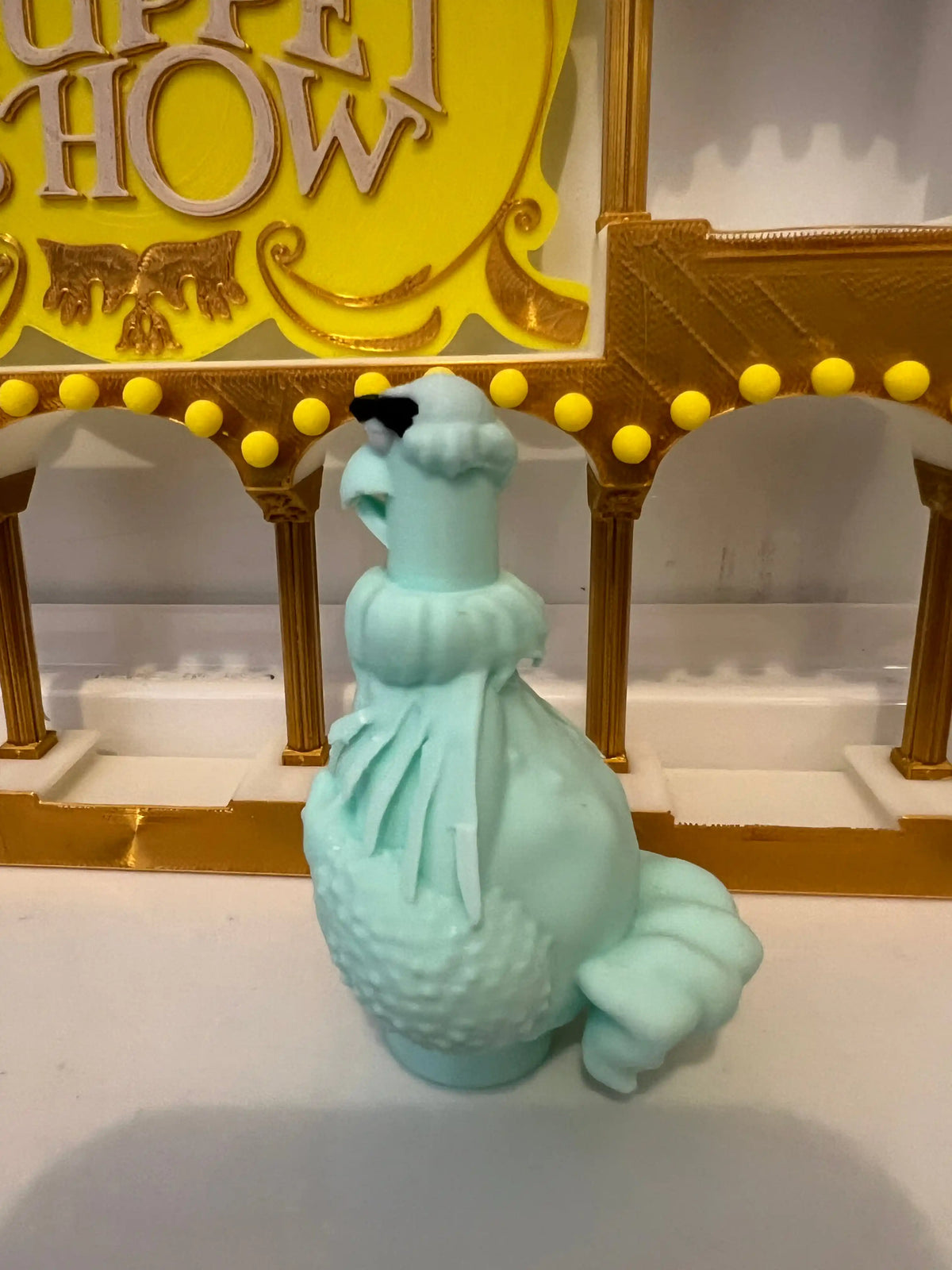 Turquoise plush eagle figurine in a frilly dress, side view with tail detail