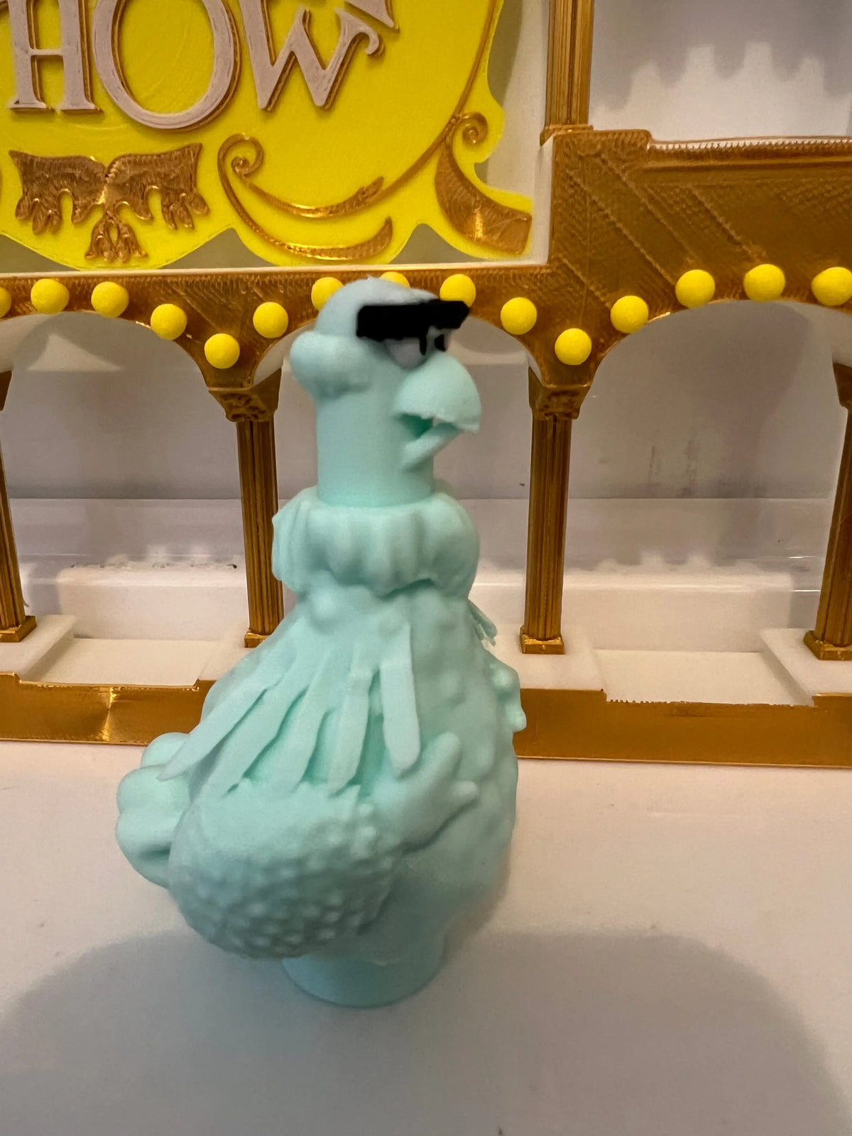 Turquoise plush eagle figurine in a frilly dress with a black tuft