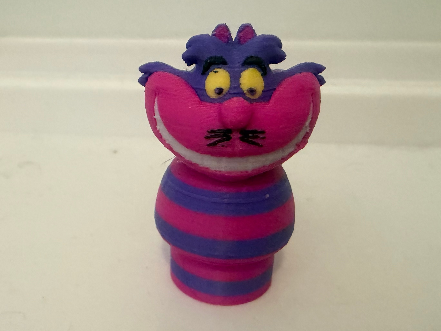 Cheshire Cat plush figure, front close-up with pink face, big yellow eyes, striped outfit