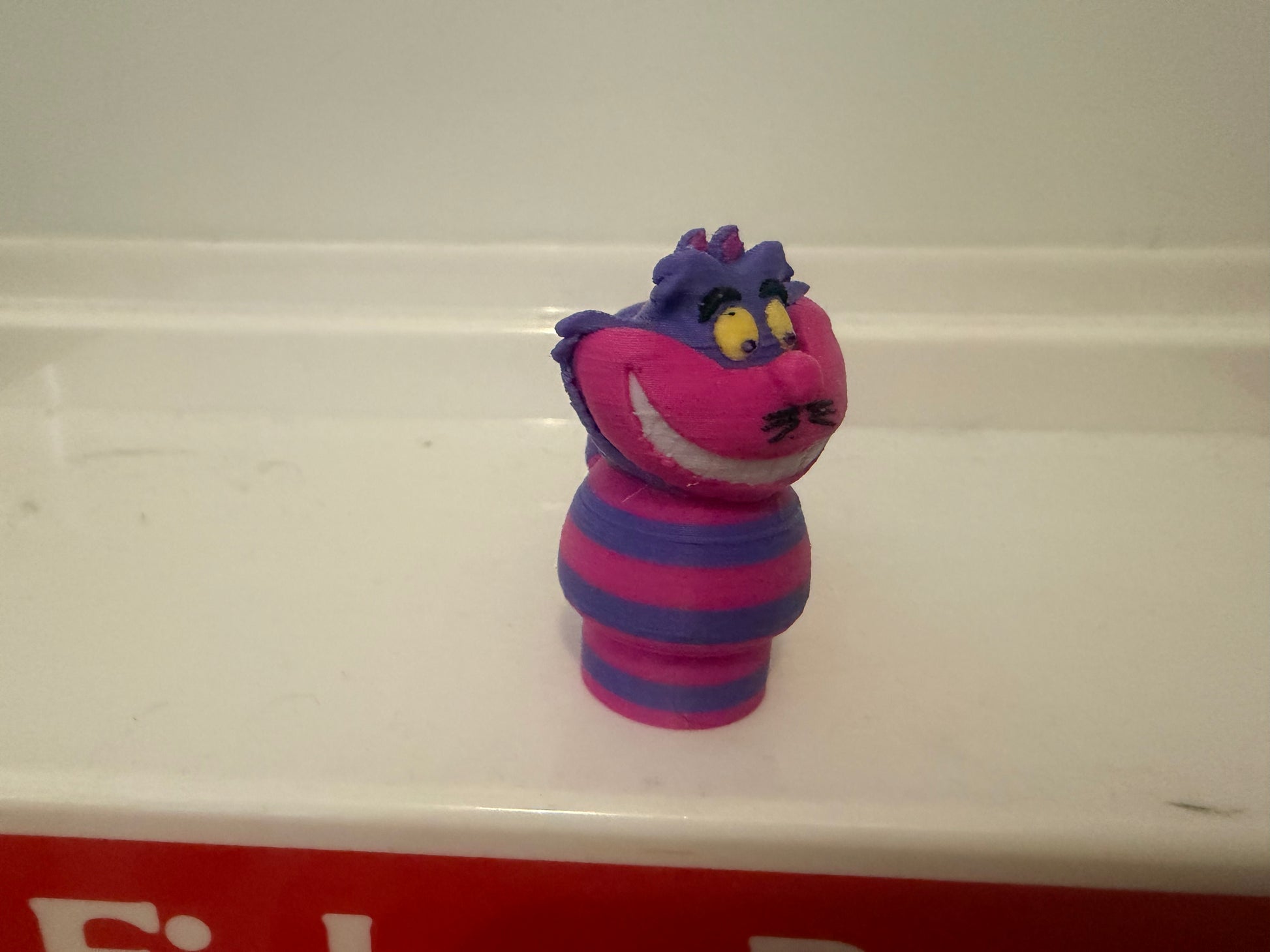 Cheshire Cat plush figure, profile view, pink grin and striped purple/blue outfit