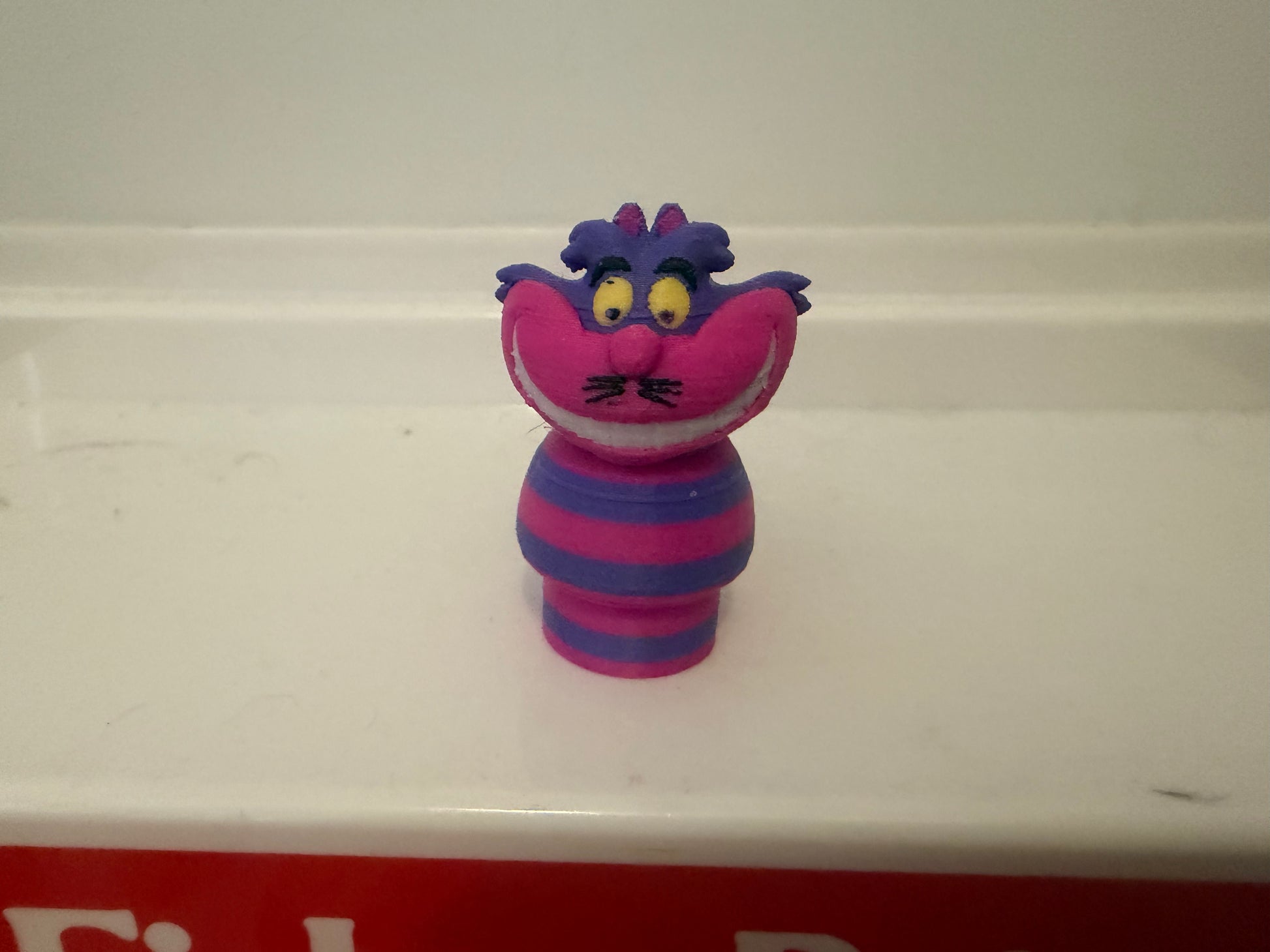 Cheshire Cat plush figure, purple head and striped blue/magenta outfit, smiling face