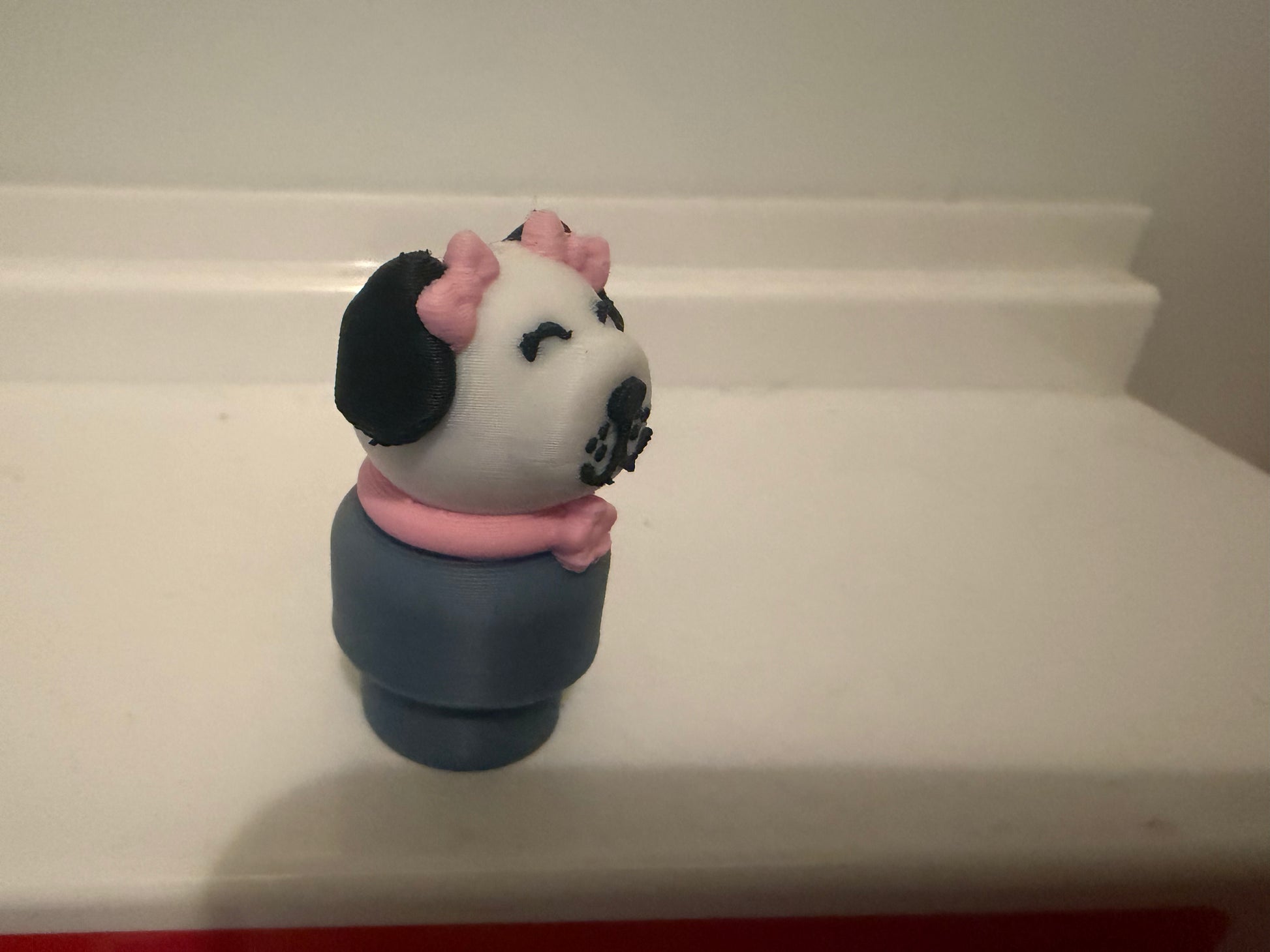 Dog figure toy with white face, pink ears, black patches, navy body, front view