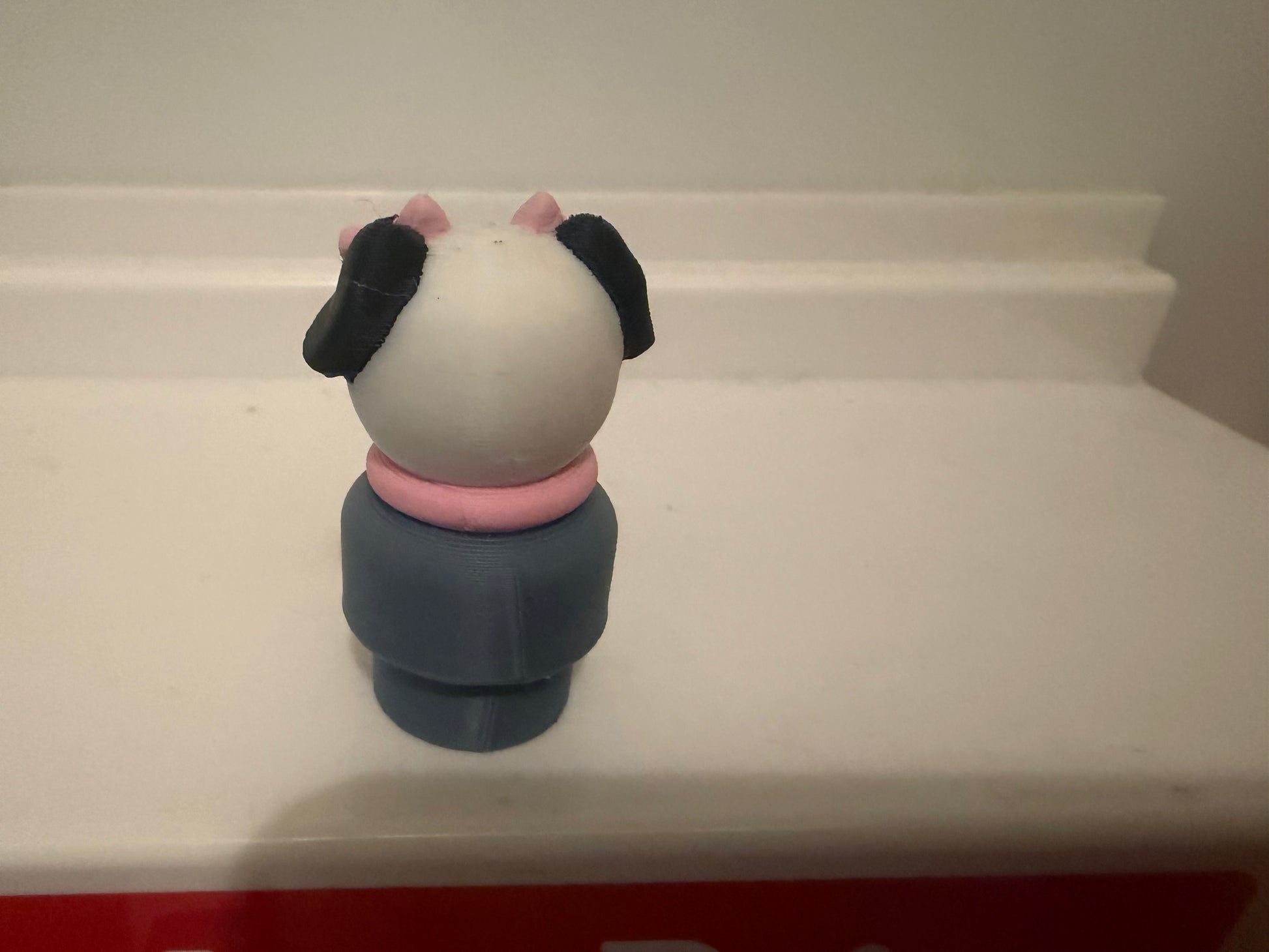 Dog figure toy with white face, black ears, pink accents, navy body, rear view