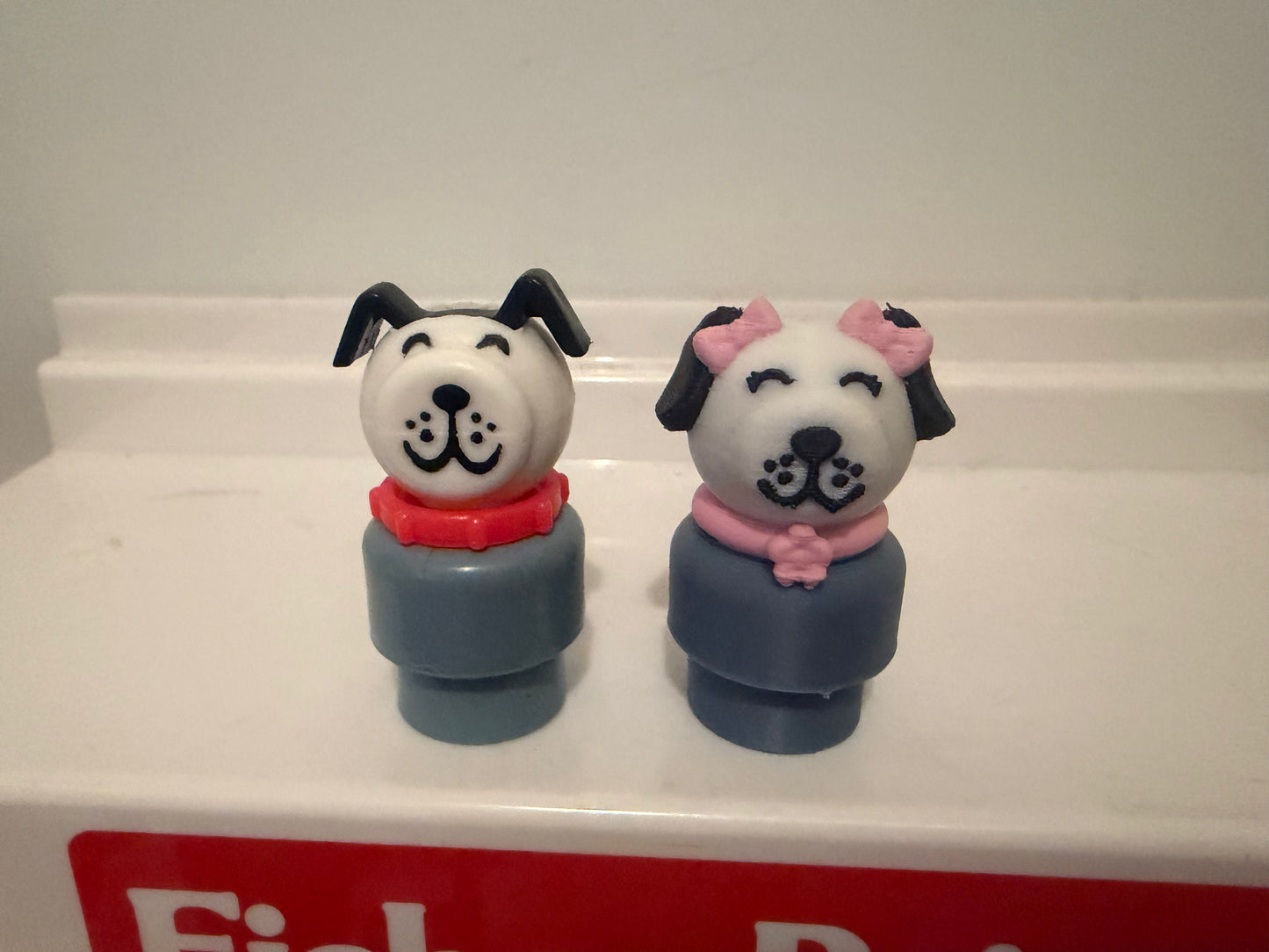 Two dog figure toys with white faces, navy bodies, pink collars, side by side