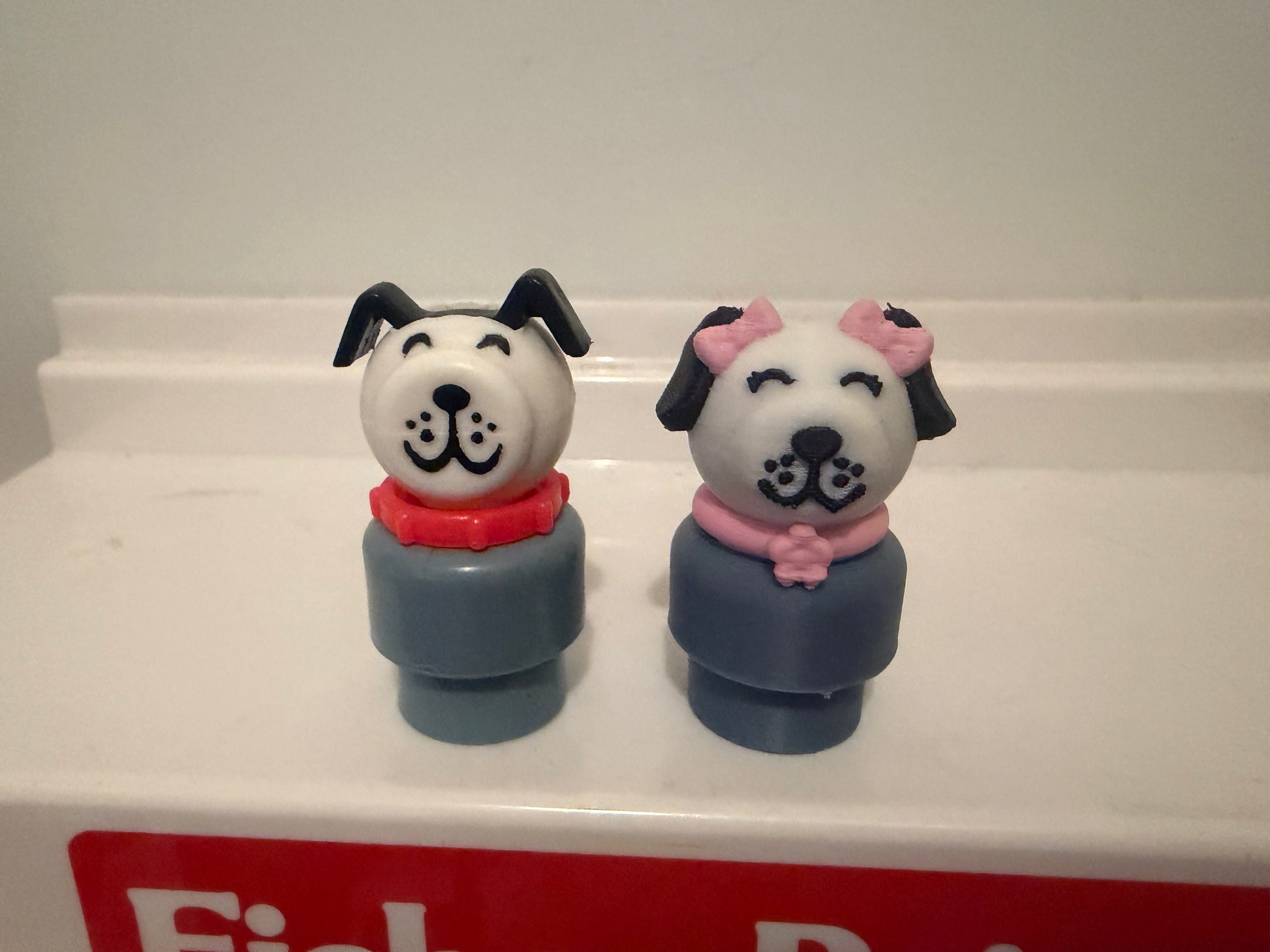 Two dog figure toys with white faces, navy bodies, pink collars, side by side