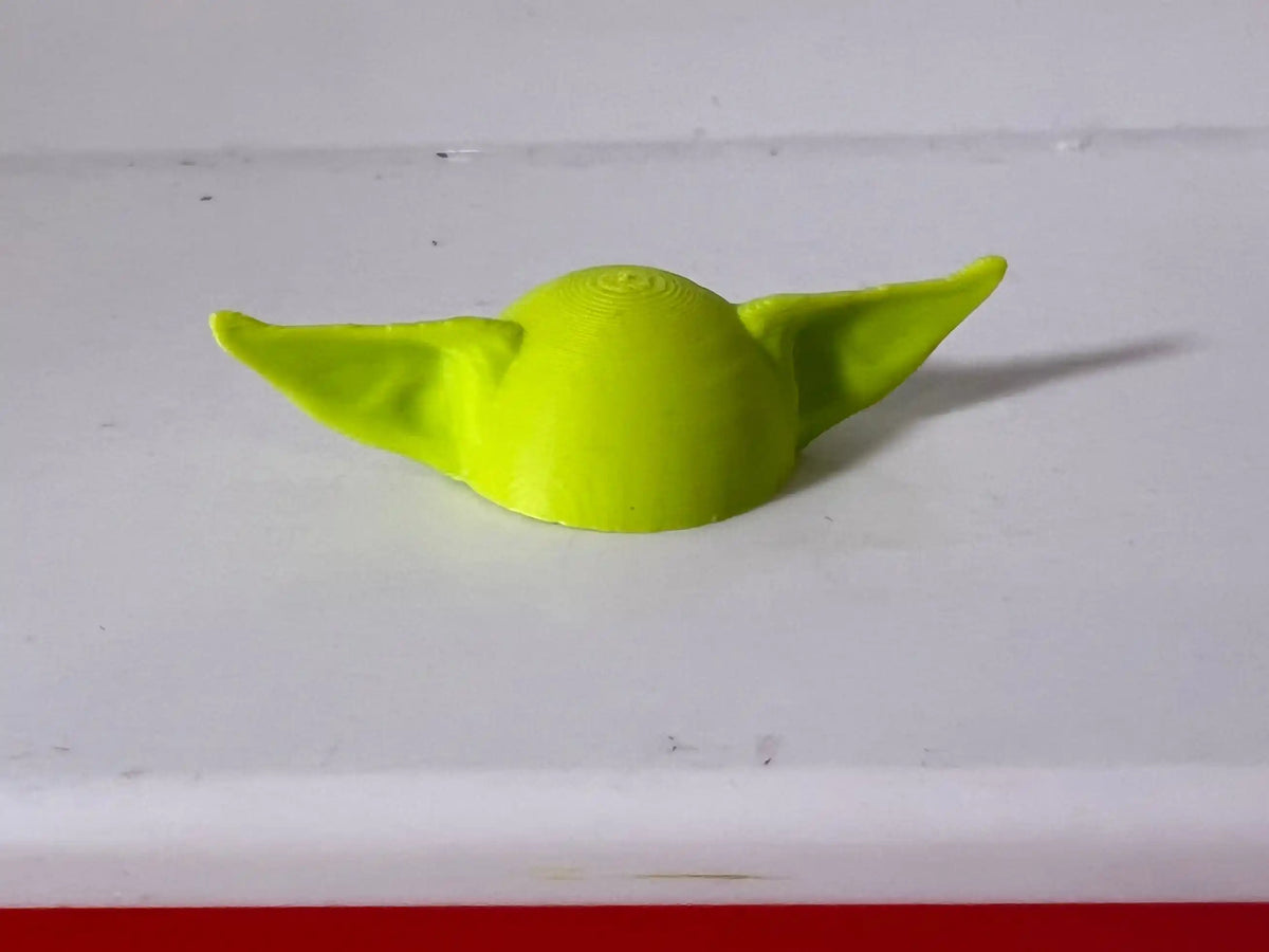 A lime green custom 3D printed Grogu hat for vintage Fisher Price Little People figures sits on a white surface.