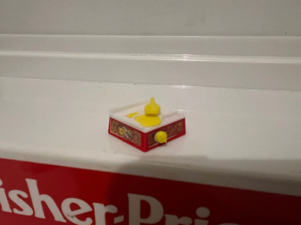 Miniature retro stove with red body and yellow knobs, small white base tray