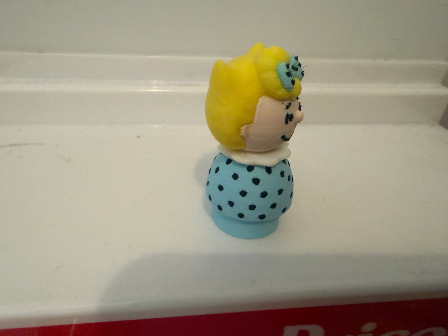 Sally Brown style 3D figure in side profile, yellow bob with blue polka-dot dress