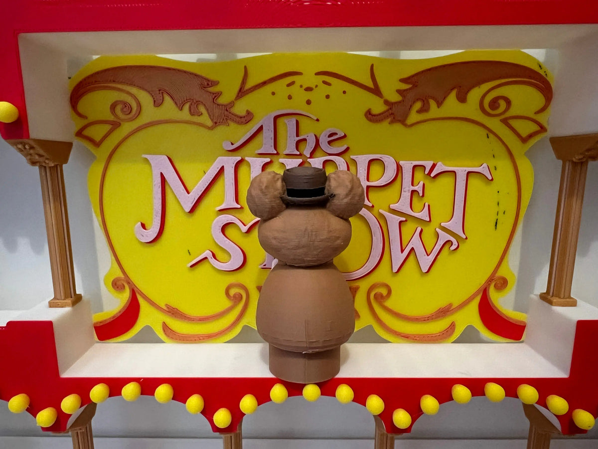 Fozzie Bear puppet figure on stage in front of yellow "The Muppet Show" sign