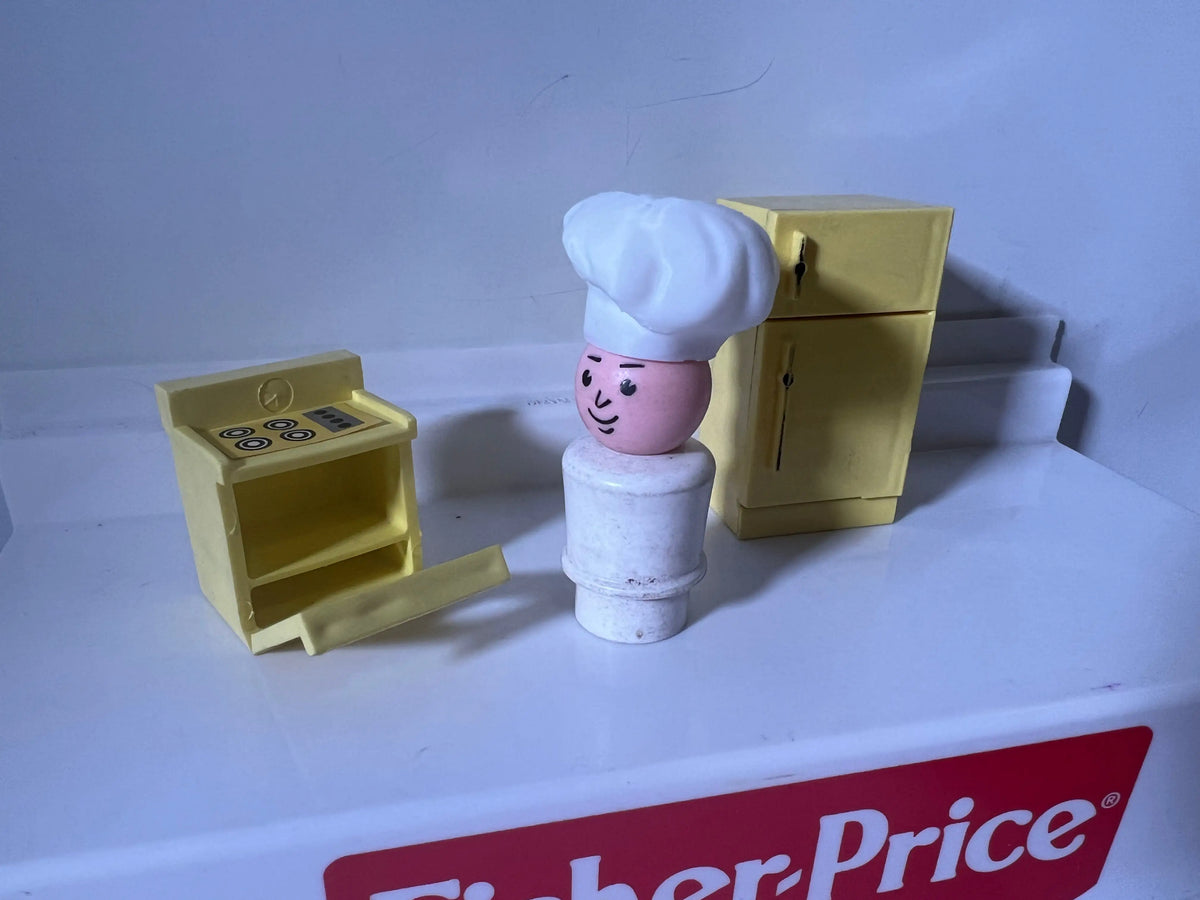 Miniature chef hat on small figure with pale face and white torso, side view