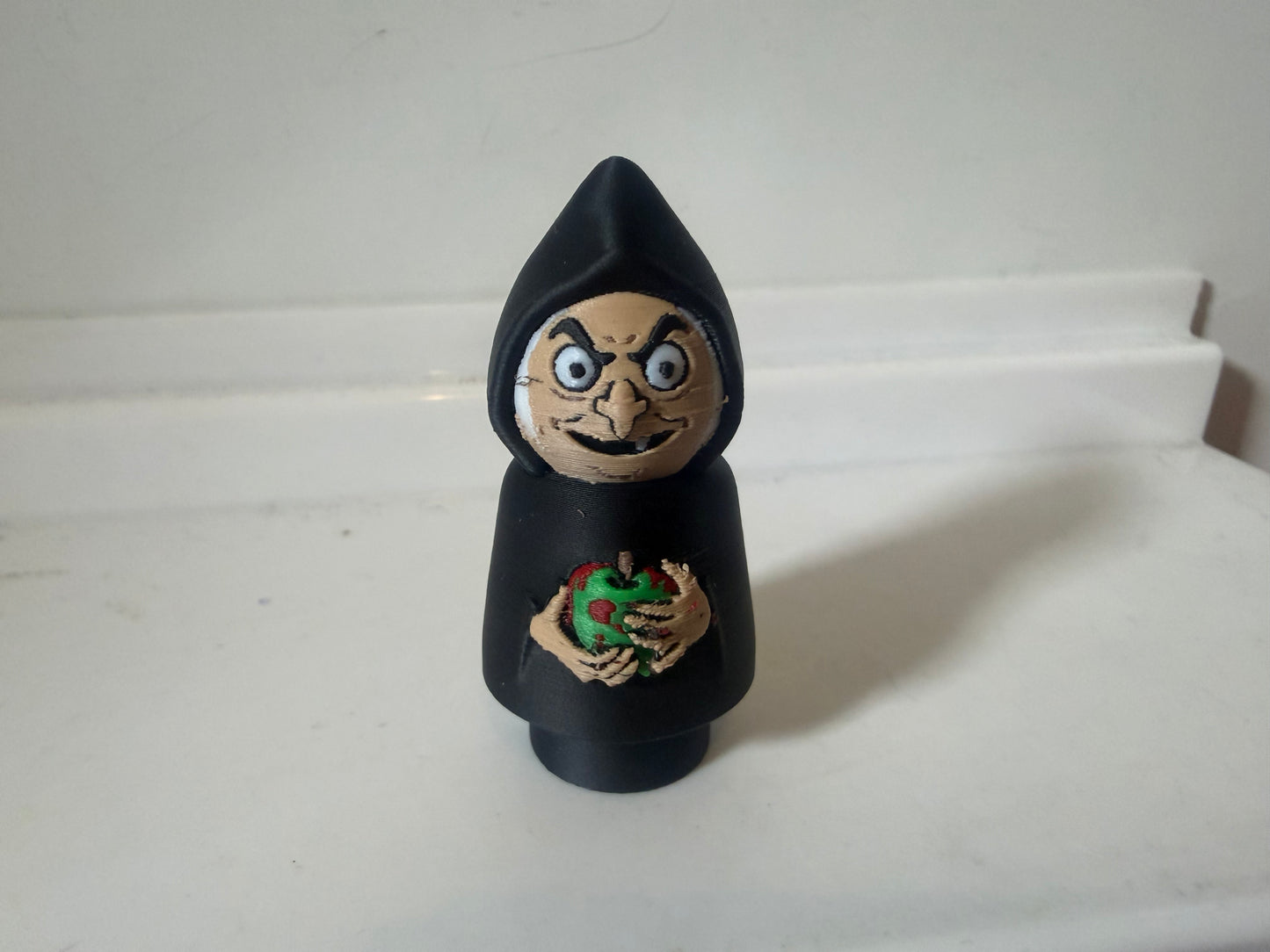 Hooded villain figure in black with smiling painted face and chest emblem