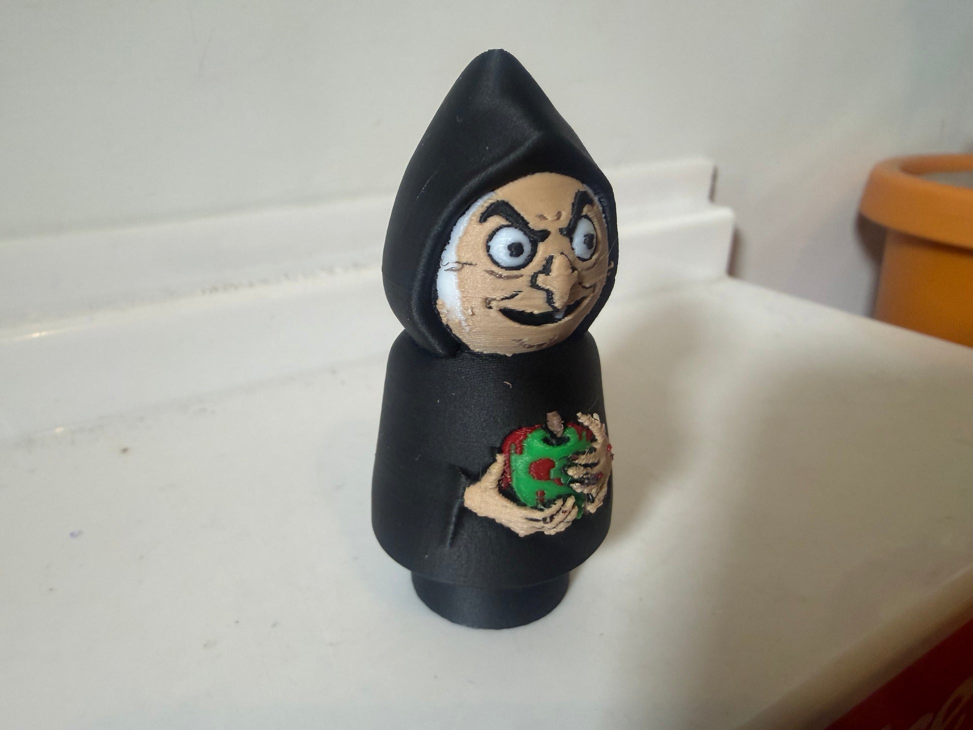 Hooded villain figure in black, angled view with wide eyes and green red chest emblem