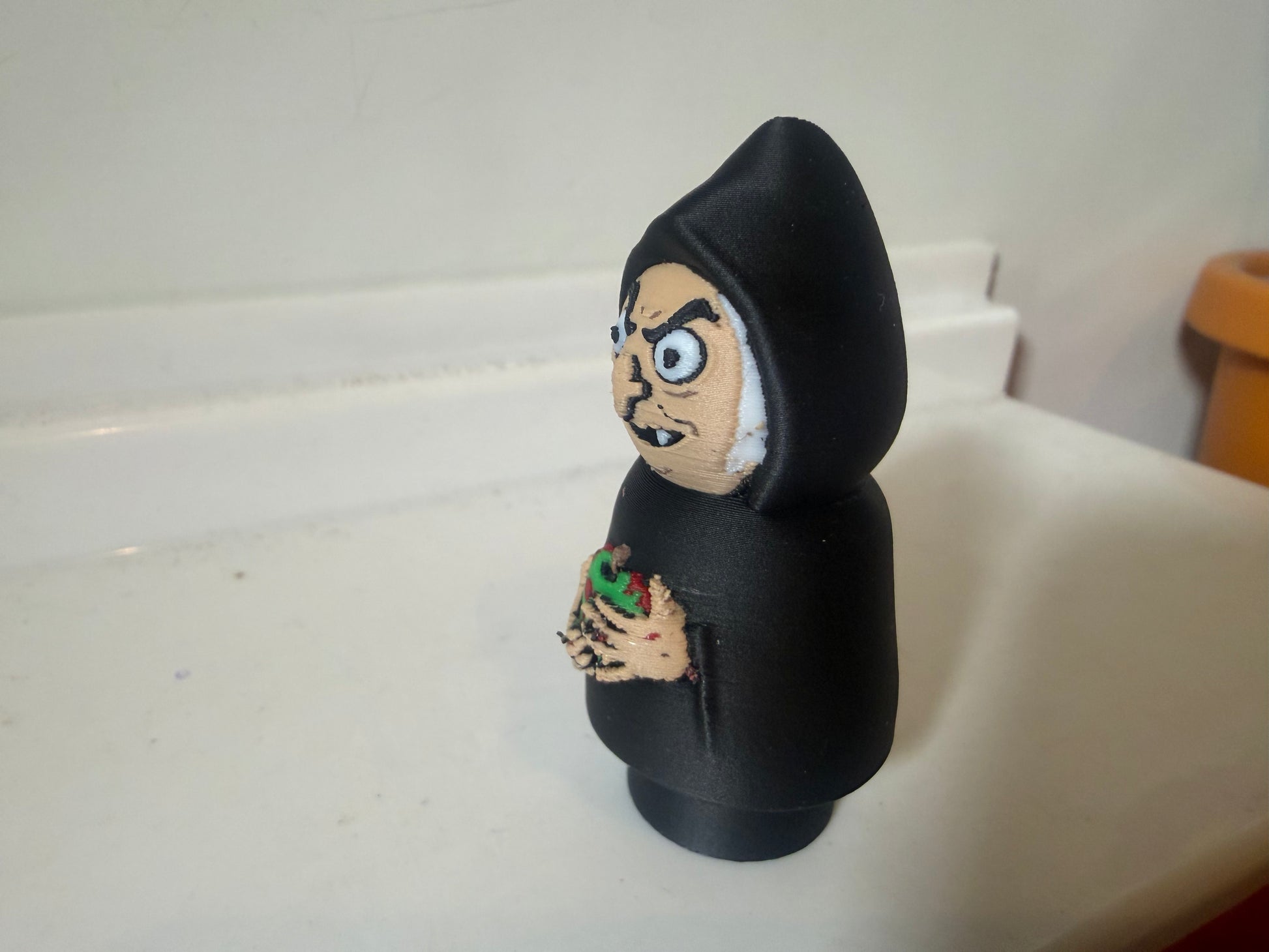 Hooded villain figure in black with painted side face and green red chest emblem