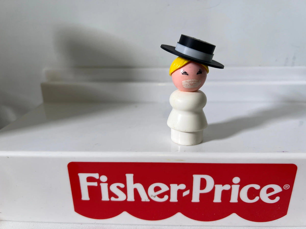 Small vintage figure wearing a black top hat with yellow hair on a white base