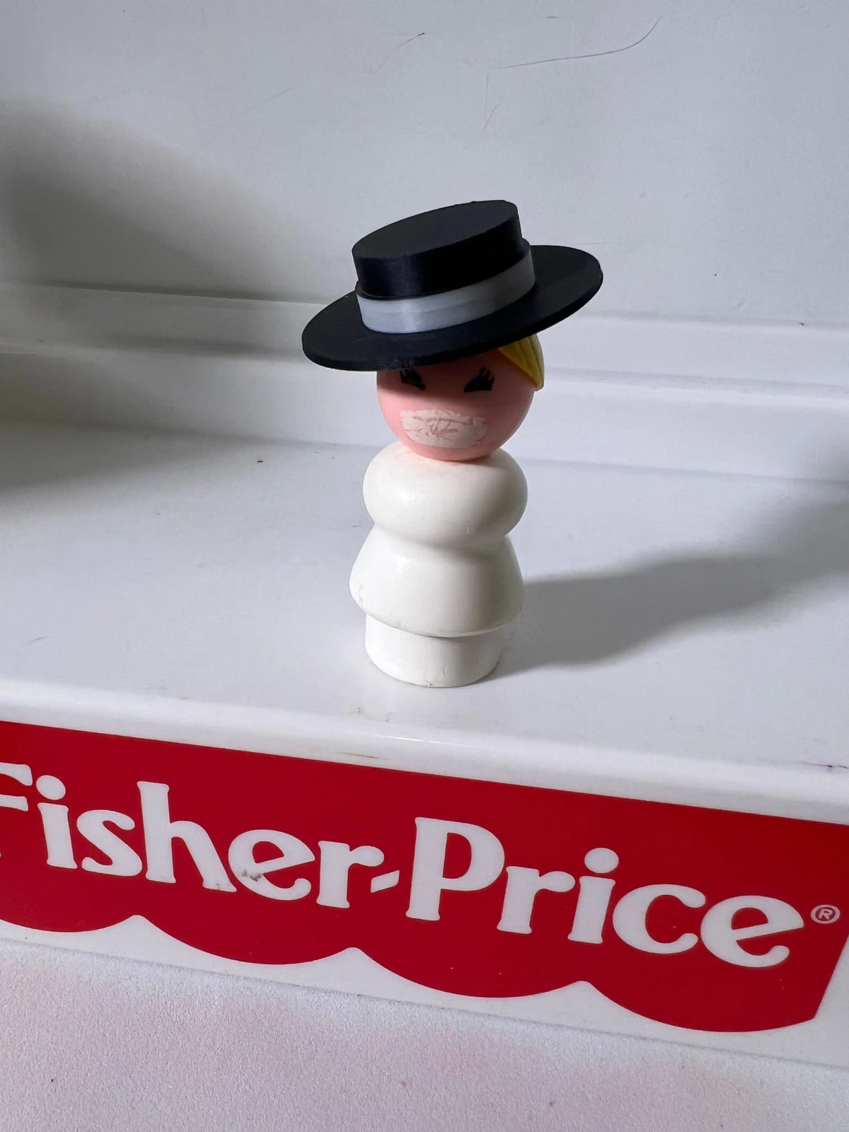 Vintage Fisher-Price figure wearing a black top hat, yellow hair visible, logo label below