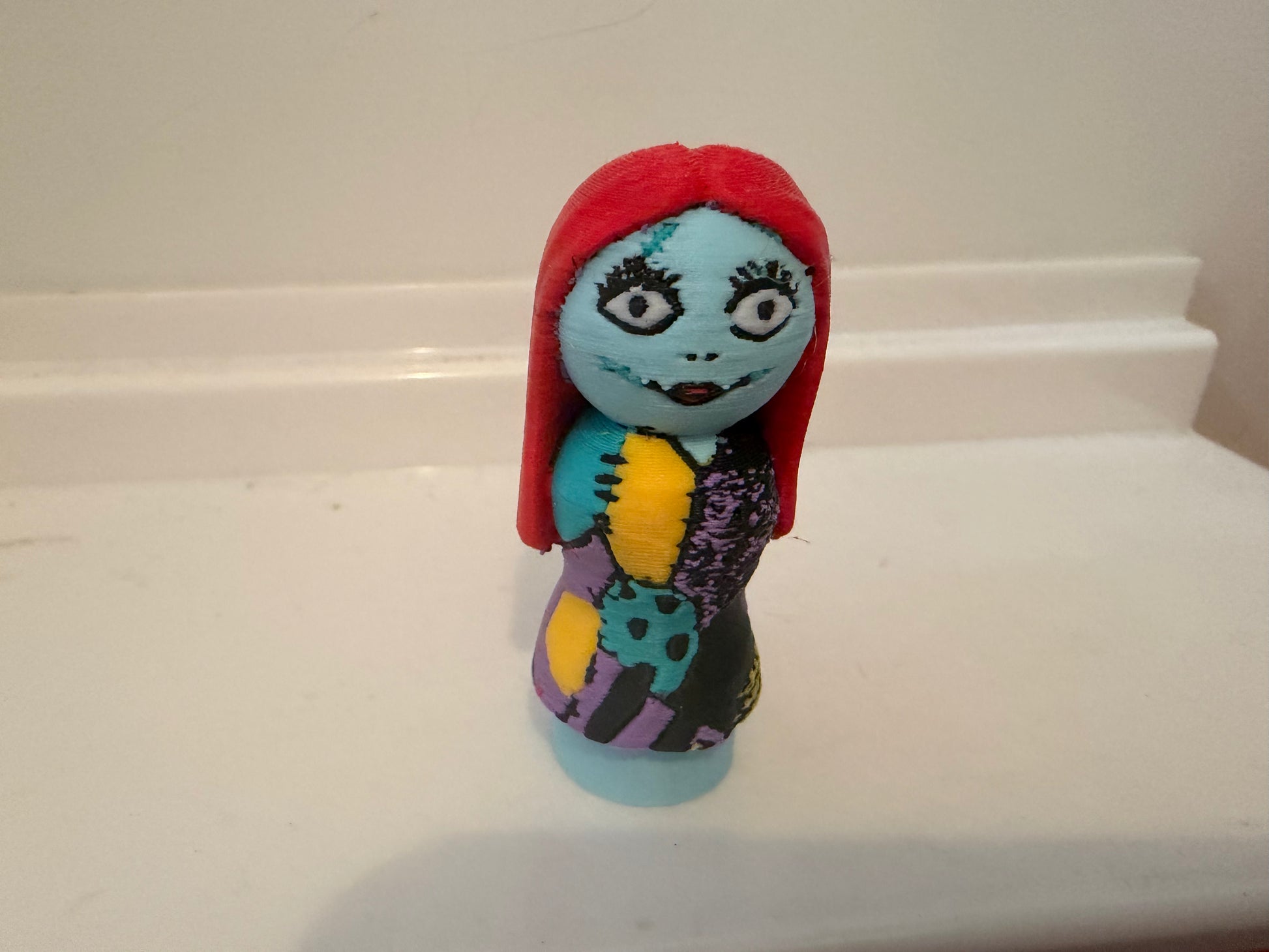Sally small figure with red hood, blue face, purple and yellow patterned dress