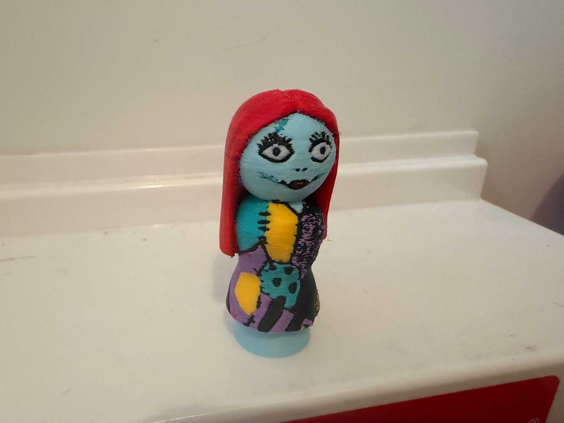 Sally figure standing upright, red hood and blue face with purple dress