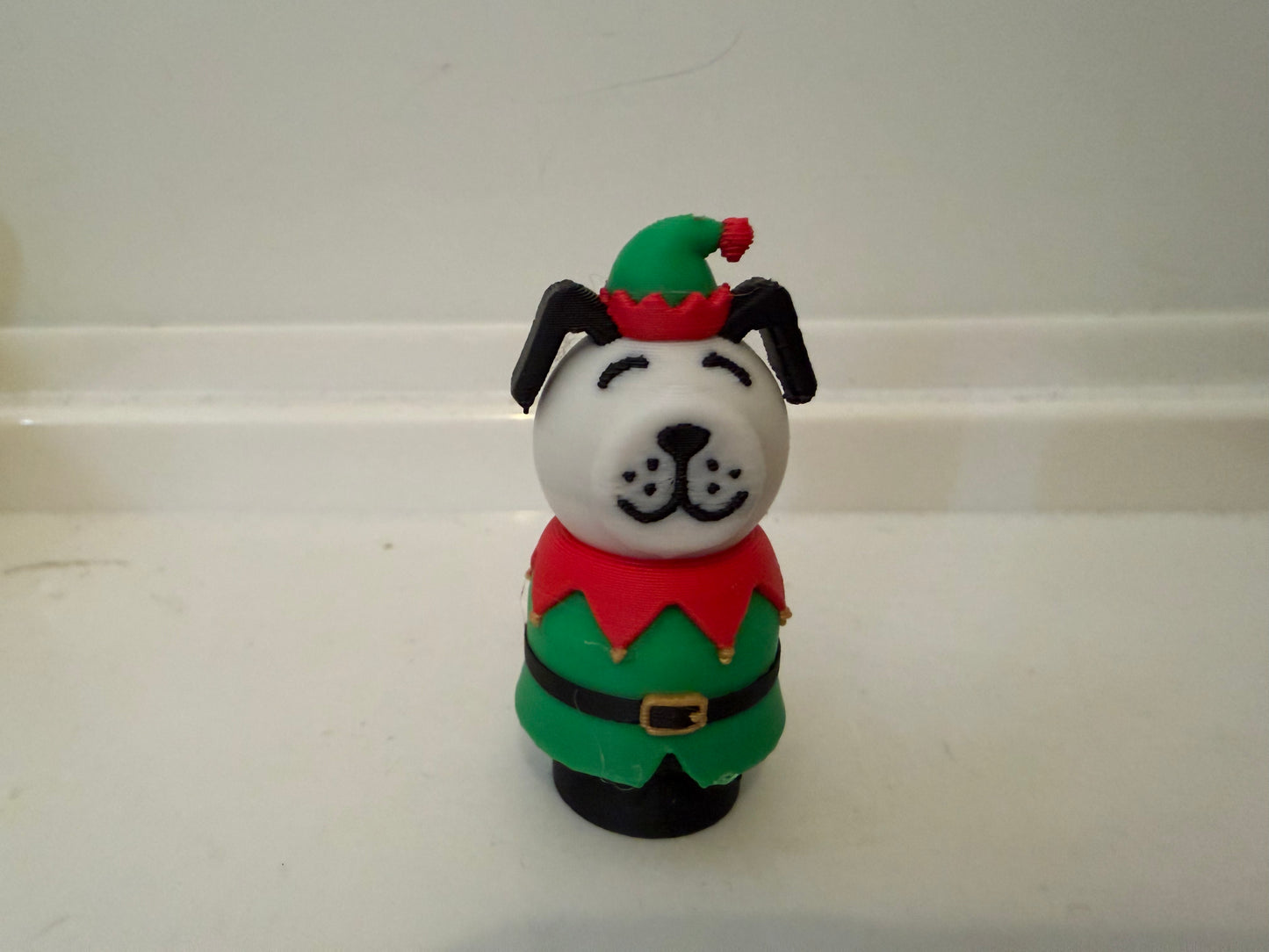 Elf-style holiday dog figurine with green hat, red shirt, and black ears