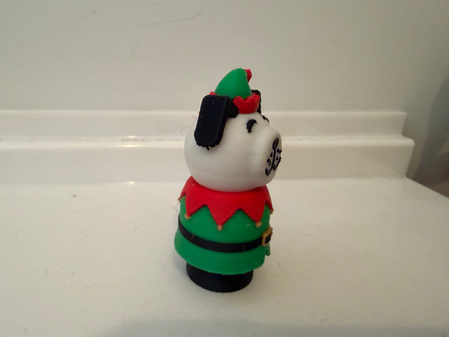 Side view of elf dog figurine in green outfit and red shirt with black ears